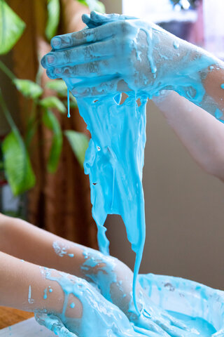 Image of two pairs of hands playing in bright blue Oobleck, an example of a non-Newtonian fluid.